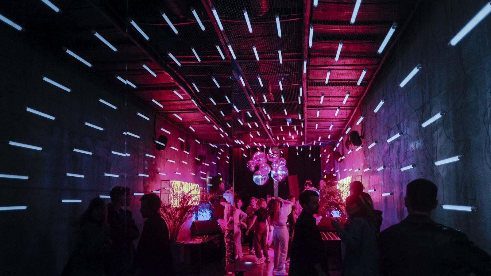 Salão de evento tomado por luzes coloridas, com convidados em uma pista iluminada.